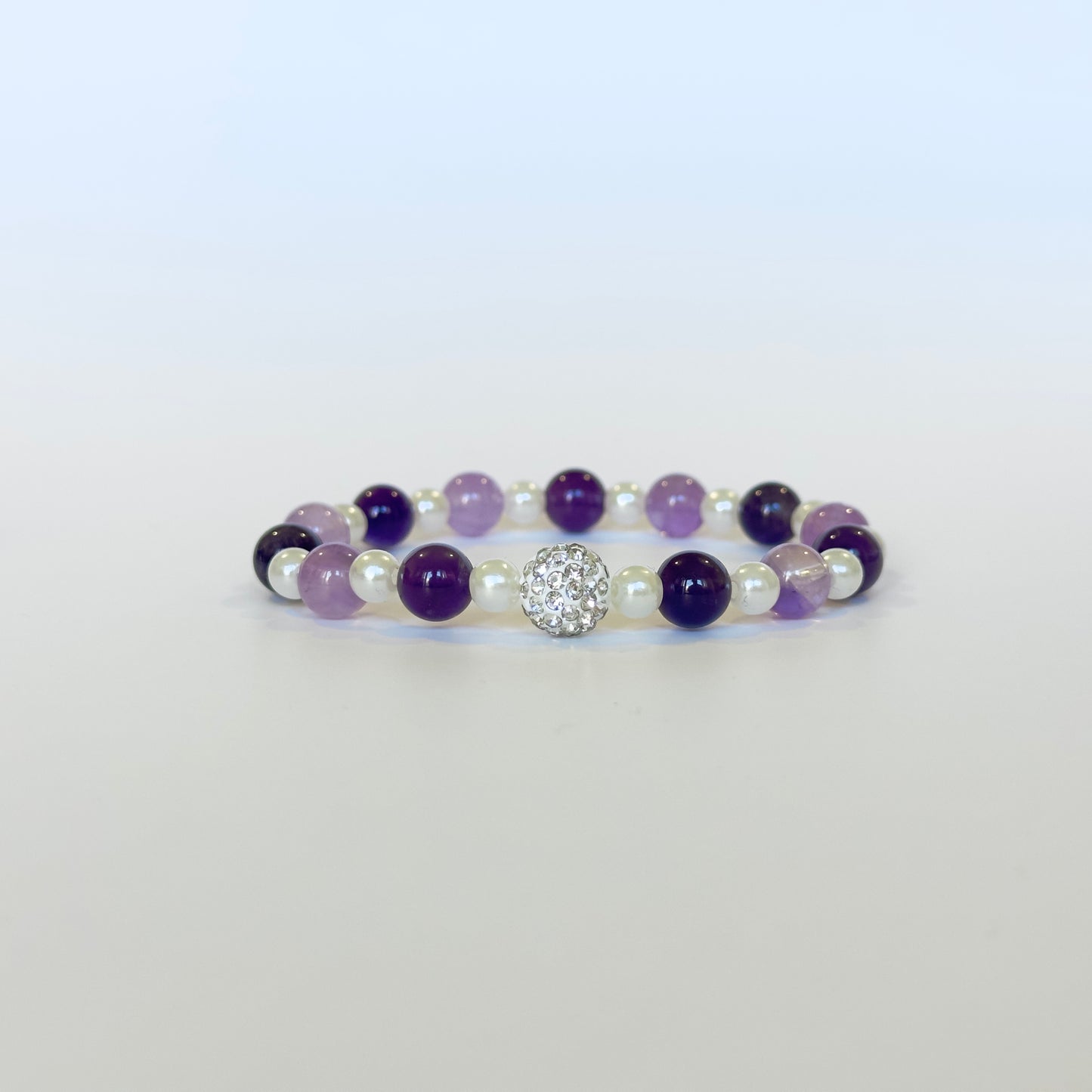 A luxurious Amethyst & Pearl Bracelet featuring deep and light Amethyst beads, luminous pearls, and a sparkling crystal charm, designed for elegance and tranquility.